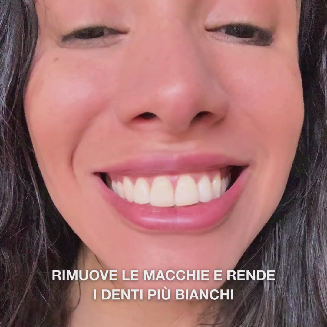 Primo piano di una mano che applica una piccola quantità di dentifricio sbiancante su uno spazzolino e spazza con movimenti circolari: la pasta fine, con silice idratata, allumina e mentolo, rimuove le macchie, rinforza lo smalto e lascia l’alito fresco 