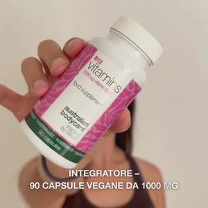 Primo piano di una mano che tiene il flacone di integratore alimentare Vitamina B12, apre il tappo e versa capsule bianche lisce—mostrando il prodotto per l’uso quotidiano a supporto di energia, sistema immunitario, sistema nervoso e riduzione della stanchezza.