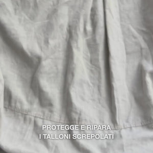 Primo piano di una mano che preleva una porzione di crema Heel Repair ricca e corposa e la massaggia delicatamente sulla pelle secca e screpolata del tallone: la consistenza densa viene visibilmente assorbita, ammorbidisce e idrata le zone ruvide mentre l’urea al 25 %, il burro di karité e l’olio di tea tree leniscono e proteggono la pelle.